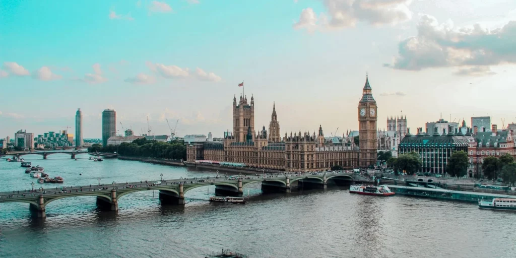 Panoramic view of the River Thames, Westminster Bridge, the Houses of Parliament, and Big Ben under a bright blue sky in London.